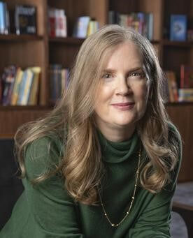 Suzanne Collins sitting in a chair looking at the viewer.