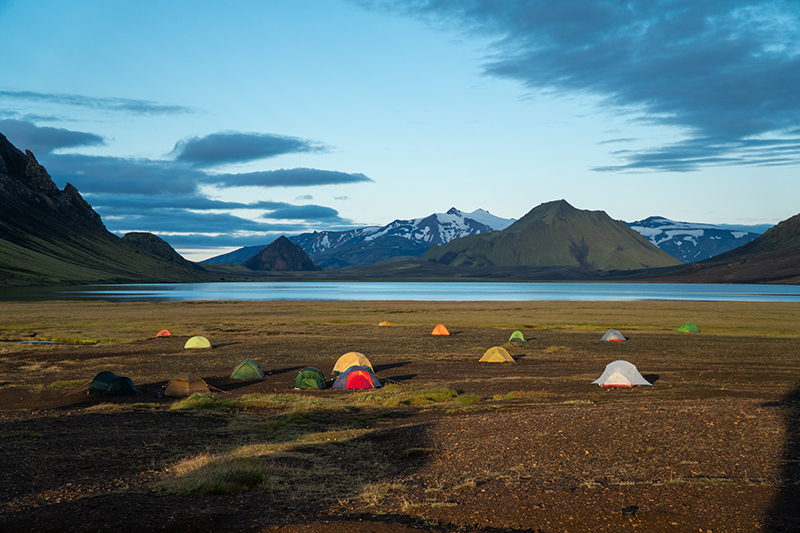 a group of tents set up in an open field surrounded by mountains and a large lake.