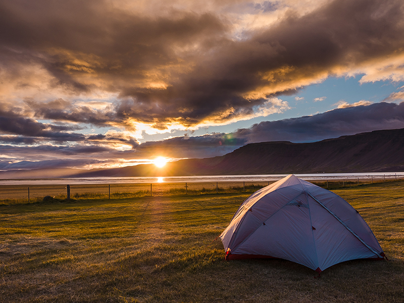 A tent is in a field with the sun setting in front of it