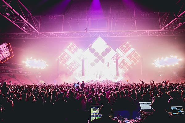 Large music venue with a show happening. Pink lights are shining bright and many people are near the stage.