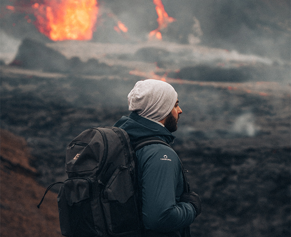 A man walks near an active volcano field, with flames and lava in the background.