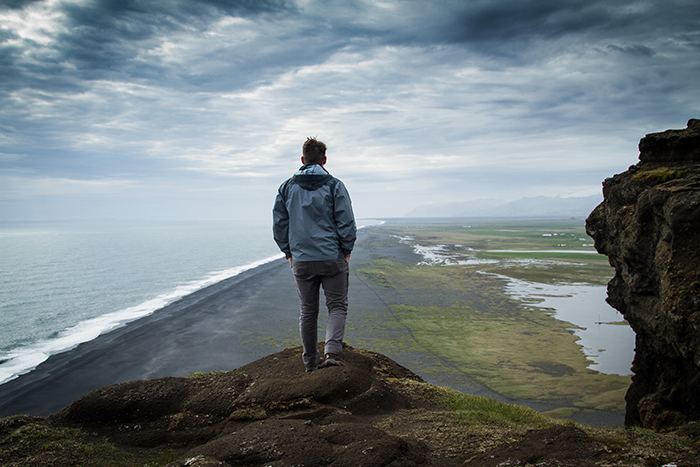 Man standing on a cliff overlooking a beach and the ocean