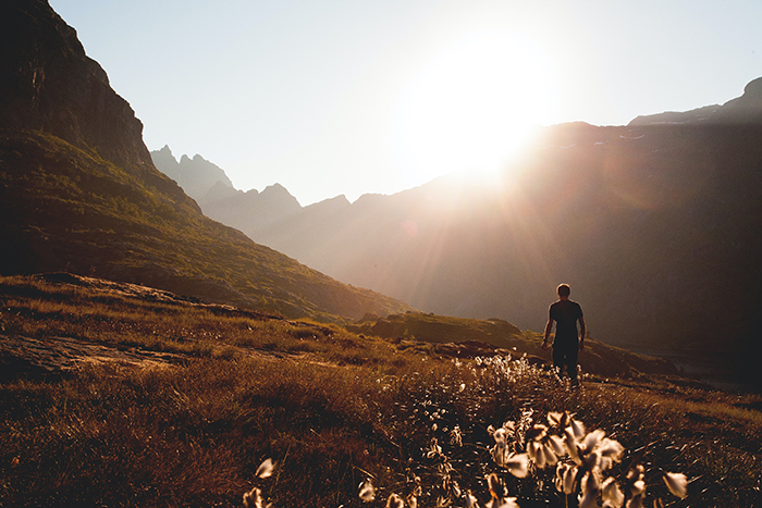 Person walking through a beautiful field surrounded by mountains during sunset