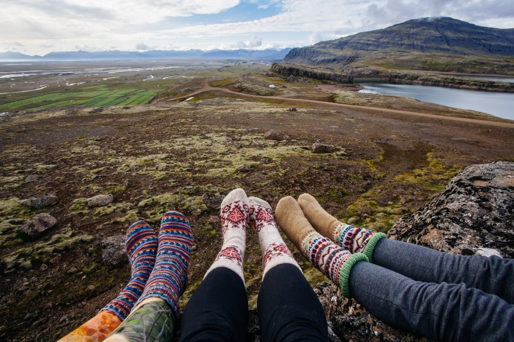 Three pairs of feet dangle from an edge showing off colorful socks with a large field below them.