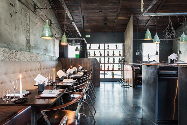 Indoor picture of a restaurant with a row of tables against a wall set with candles and menus.