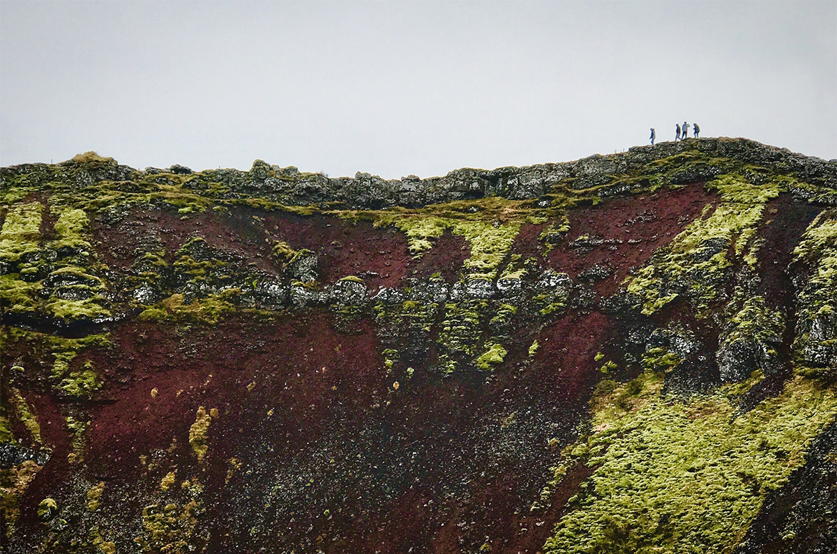 People walk atop a very tall mountain trail in the distance.