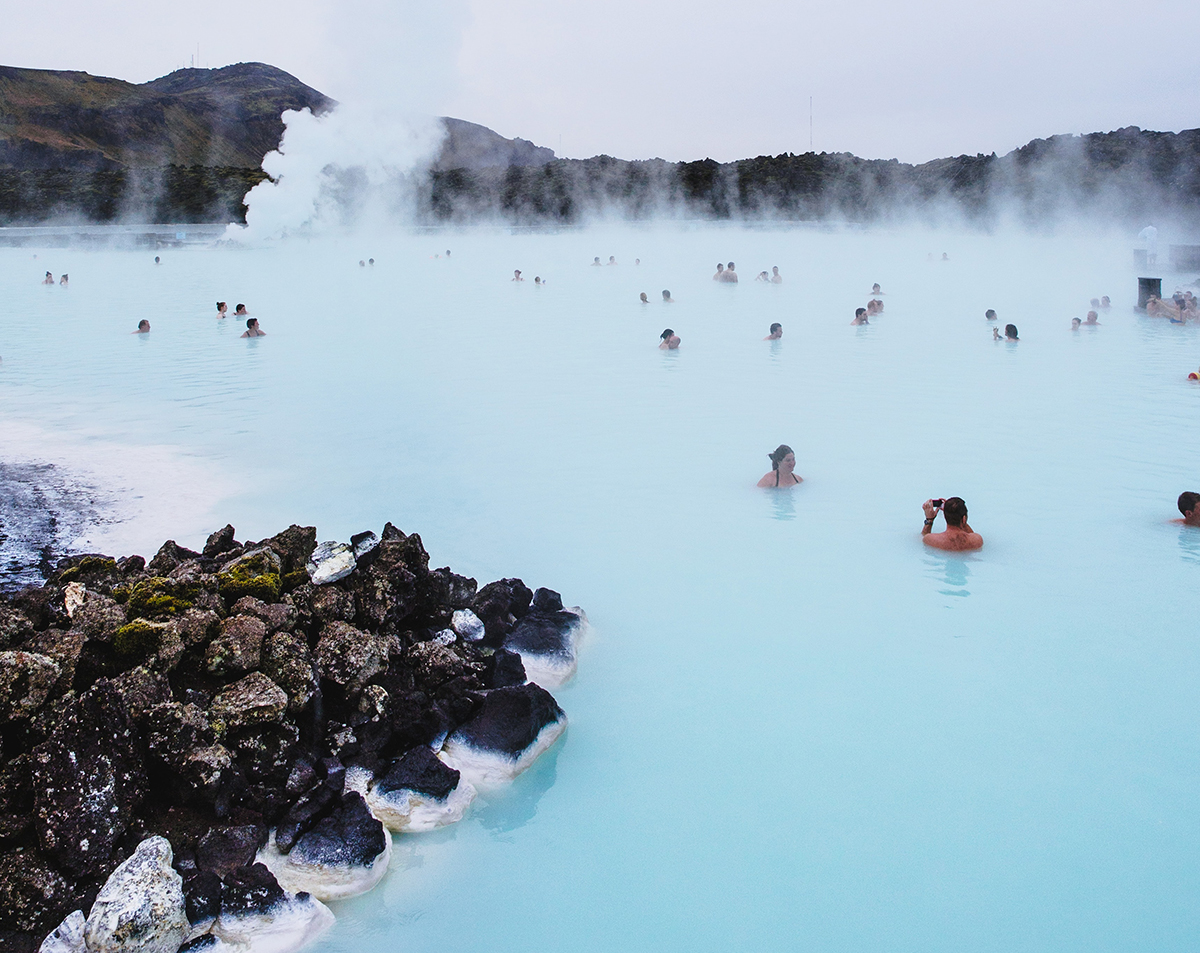 People bath in a natural hotspring with steam coming off the water.