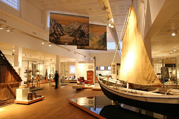 Indoor photo of the National Museum of Iceland showcasing different artifacts. A sailboat sits in the room with its sails raised.