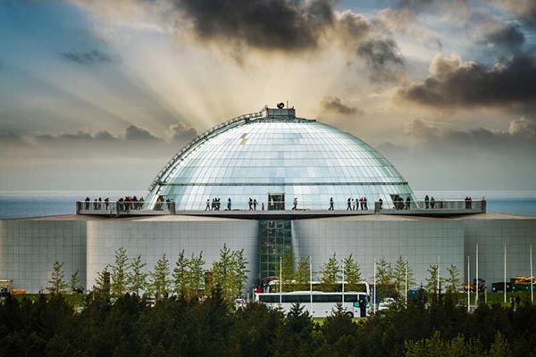 Ground view image of the Perlan Museum with rays of the setting sun behind it.