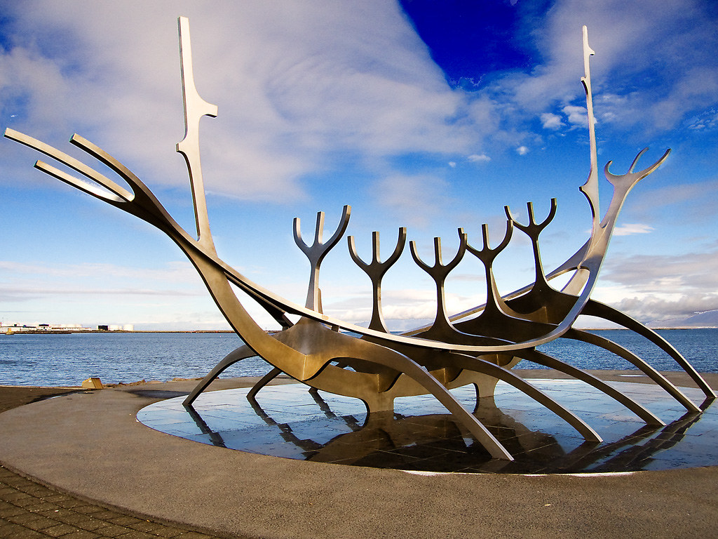 A beautiful modern sculpture of a viking ship stands near the ocean.